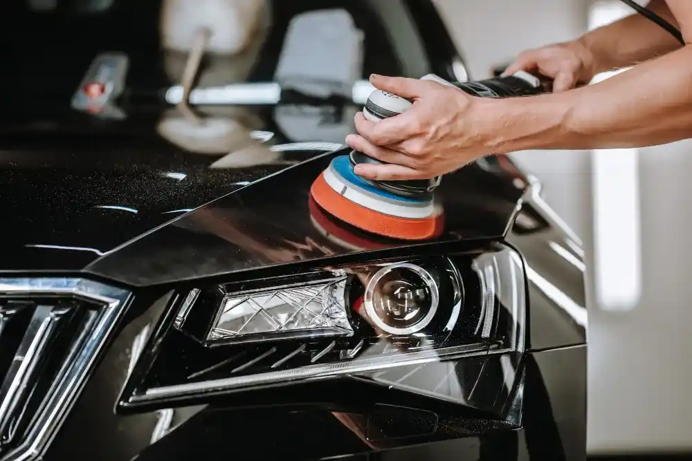 Detailer using a dual-action polisher on a black car's hood and headlight during the paint correction process
